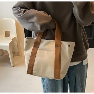Detailed view of canvas tote bag featuring brown woven handles and metal rivet reinforcement