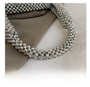 Detailed close-up of metallic silver beaded handle on a woven evening handbag