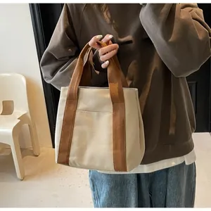 Detail view of beige canvas tote bag with brown woven handles and front pocket