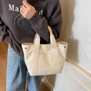 Detail of a beige canvas tote bag with metal buckle and functional front pocket