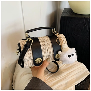 Detail of woven straw handbag with black leather flap and cute plush cat charm