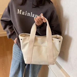 Detail view of cream canvas tote bag with thick handles and front patch pocket design