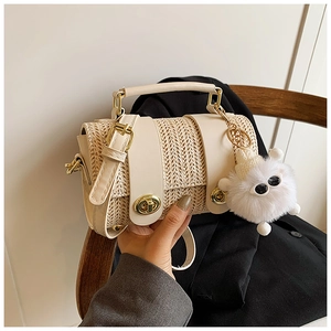 Detail of beige straw handbag with leather trim, gold hardware and furry monster charm