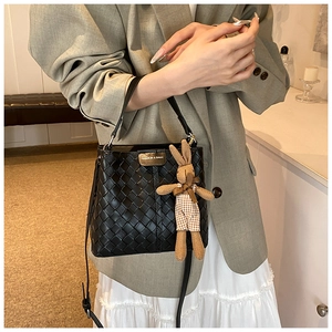 Detail of black woven bucket bag with metal logo plate and cute rabbit plush charm