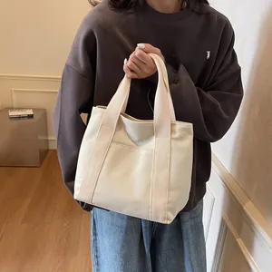 Close-up of cream canvas tote bag showing the front pocket design and wide strap detail