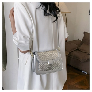 Detail of silver woven crossbody bag with metallic texture and golden buckles on model