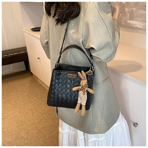 Detail of black woven leather bucket bag featuring a cute bunny charm and metal logo