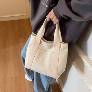 Detail of off-white canvas tote bag featuring double handles and front pocket for daily commute