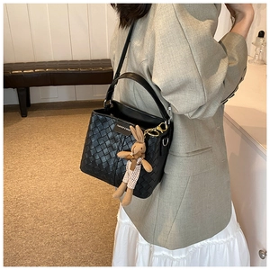 Detail of black woven leather bucket bag with cute rabbit pendant and fashion logo tag
