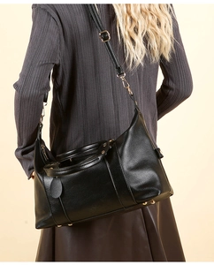 Détail d'un sac à bandoulière en cuir grainé noir avec ferrures dorées porté par un modèle