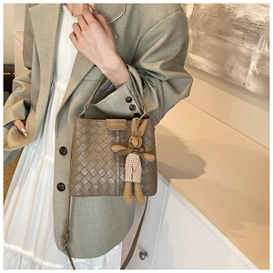 Detail of woven khaki bucket bag with cute bunny charm and branded leather patch