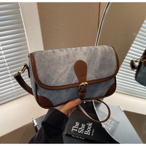 Détail du sac bandoulière en denim bleu avec des finitions en cuir marron