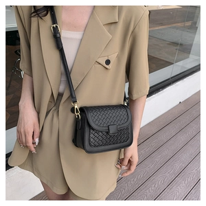 Detail of black woven leather flap bag with gold metal buckle and adjustable strap