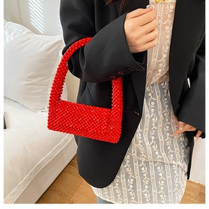 Detail of red handmade beaded shoulder bag with textured woven surface on black blazer