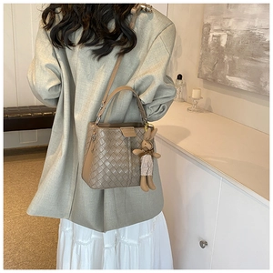 Detail of woven bucket bag in taupe with cute bunny charm on a beige suit