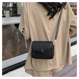 Detail of black woven texture crossbody bag shown on a model with golden metal hardware
