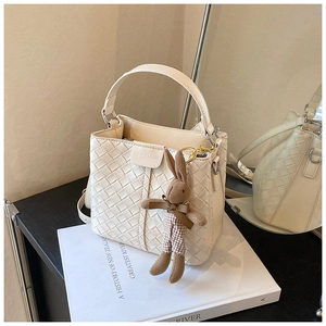 Detail of cream woven bucket bag with leather texture and cute rabbit charm on books