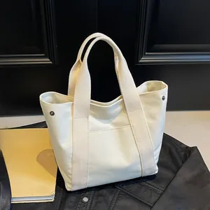 Detail shot of a cream canvas tote bag showing the side metal snaps and front slip pocket