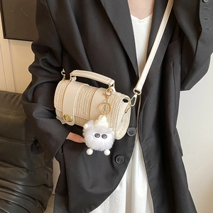 Beige woven cylinder crossbody bag with leather trim and plush charm for spring style