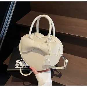 Close-up of white heart-shaped handbag featuring a large bow and elegant heart pendant