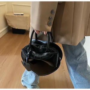 Detail of a heart-shaped black leather handbag with a bow and matching charm