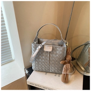 Close-up of woven silver bucket bag with bunny pendant and elegant metal logo detail