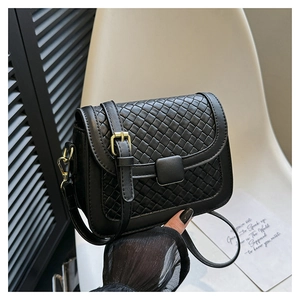 Detail of black woven leather crossbody bag featuring gold buckle and textured flap surface