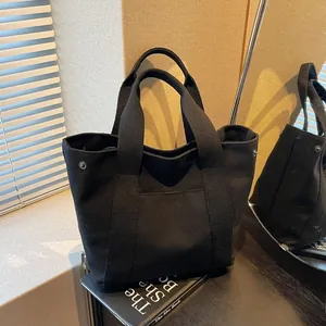 Detail of black canvas tote bag with reinforced handles and side metal snap buttons
