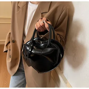 Detail of a black heart-shaped shoulder bag with a large bow and glossy finish
