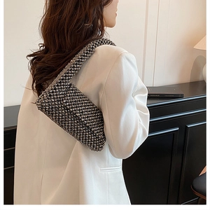 Close-up of a dark grey beaded shoulder bag with a metallic finish on a white blazer