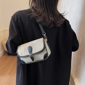 Sac à bandoulière texturé gris avec garniture en cuir noir et boucle dorée porté par mannequin