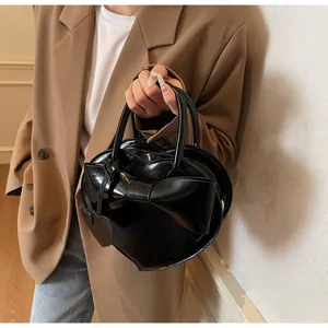 Detail of a black heart-shaped handbag with a large bow and glossy patent leather finish