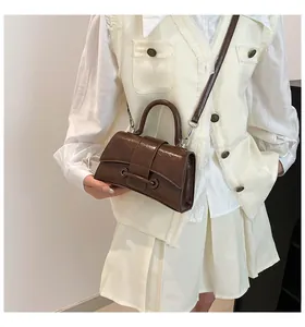 Detail of dark brown hourglass handbag with glossy finish and top handle on a model