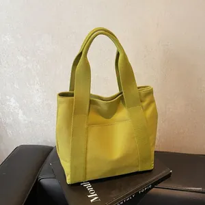 Detail of a mustard green canvas tote bag with front pocket on a black leather seat