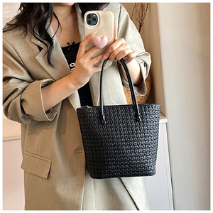Detail view of a black woven tote bag featuring glossy leather shoulder straps on a model