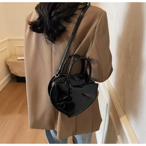 Detailed view of black heart-shaped bag with bow and charms worn by a model in a brown suit