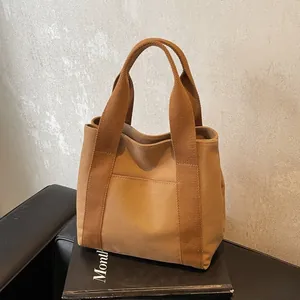 Close-up of a camel canvas tote bag with dual handles and front pocket on a book