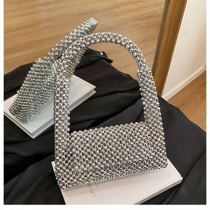 Close-up of a silver beaded handbag with a curved top handle and metallic reflective finish