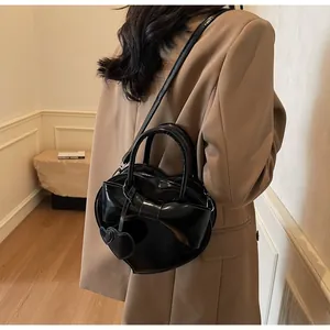 Detail of a black heart-shaped handbag with a large bow worn with a brown blazer jacket