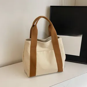 Detail of cream canvas tote bag featuring brown ribbon handles and front pocket