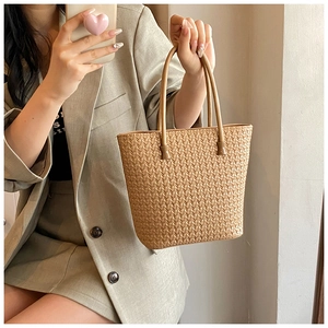 Detail of a minimalist beige woven shoulder bag featuring long straps and trapezoid structure