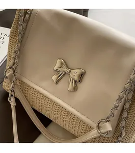 Détail du sac cabas en paille tissée beige avec nœud doré et bandoulière en chaîne