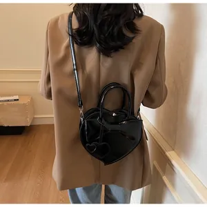 Detail of a black heart-shaped handbag with a large bow and slim shoulder strap on a model