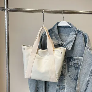 Detail showing cream canvas tote bag with metal rivets hanging on a garment rack