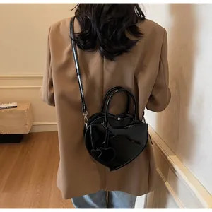 Detail of black heart-shaped shoulder bag featuring a large bow and glossy finish