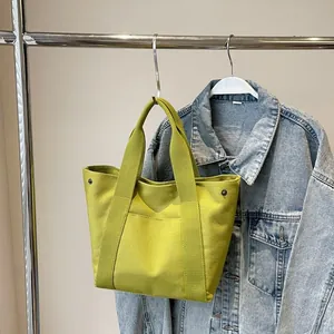 Detail of green canvas tote bag with front pocket and decorative metal rivets