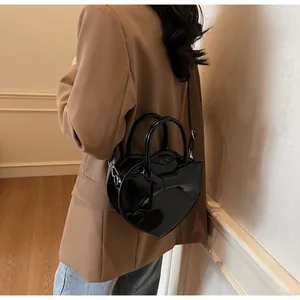 Detailed view of black heart-shaped handbag with glossy finish and large bow accent