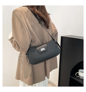 Side view of black leather underarm bag with silver buckle worn with a brown blazer