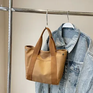 Detail of a brown canvas tote bag with wide straps and metal rivets on a coat rack