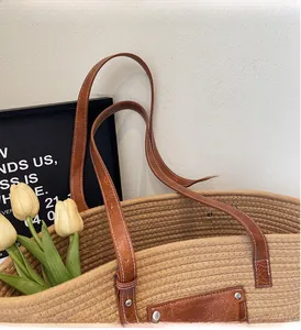 Close-up of woven straw tote bag featuring brown faux leather handles and contrast stitching